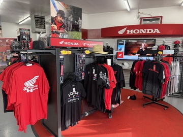 Honda apparel display with red and black shirts, hats, and accessories inside the Hamburg Honda showroom.