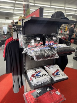 helves of folded HRC hoodies and Honda logo shirts along with hats and jackets in the showroom.