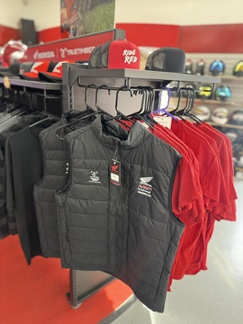 Close-up of TrueTimber padded vests and Honda Ride Red hats on a showroom apparel rack.