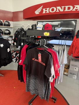Rack of Honda shirts, red and black tees, and FOX hats with a Honda wall display in the background.