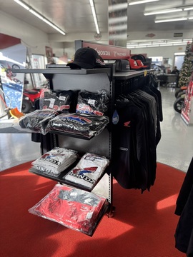 Rack of Honda shirts, red and black tees, and FOX hats with a Honda wall display in the background.