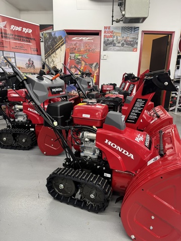 Row of Honda HSS724ATD, HSS928ATD, and HSS1332ATD track-drive snowblowers displayed inside Hamburg Honda showroom.